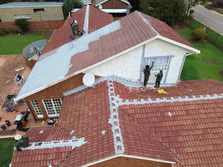 Two painters working on a white gable end with tins and tools below