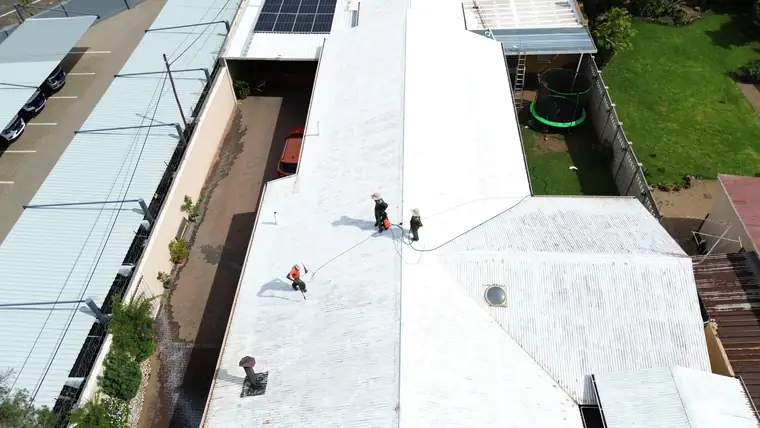 Three crew spraying white coating along a long commercial roof